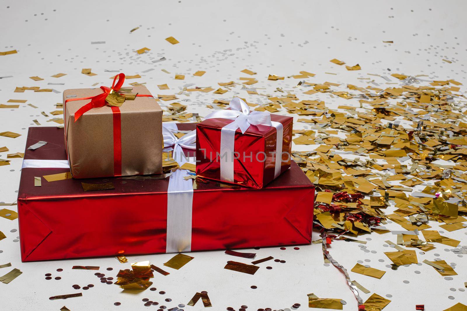 Floor covered with gold confetti. Big gift box on the floor with two smaller presents on the top of it. New year and happy holiday concept