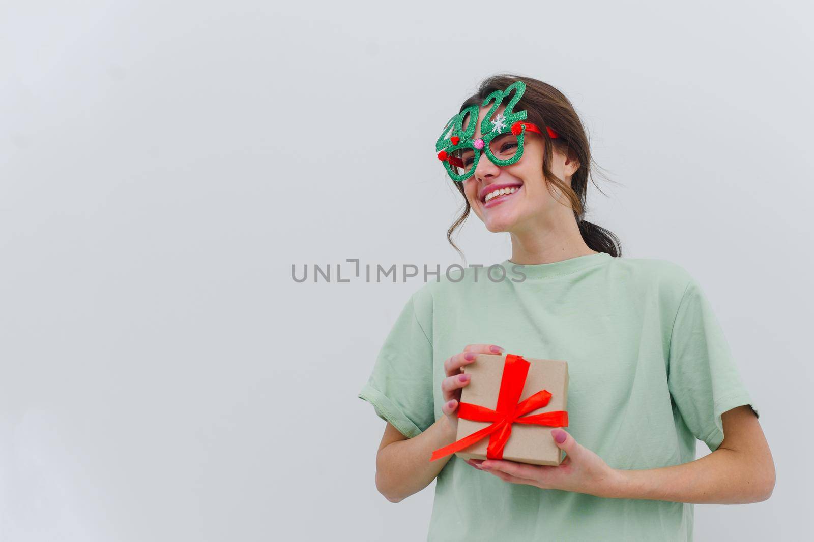 Photo of an excited young woman wearing 2022 Christmas tree glasses, isolated on a white background. Copy space.