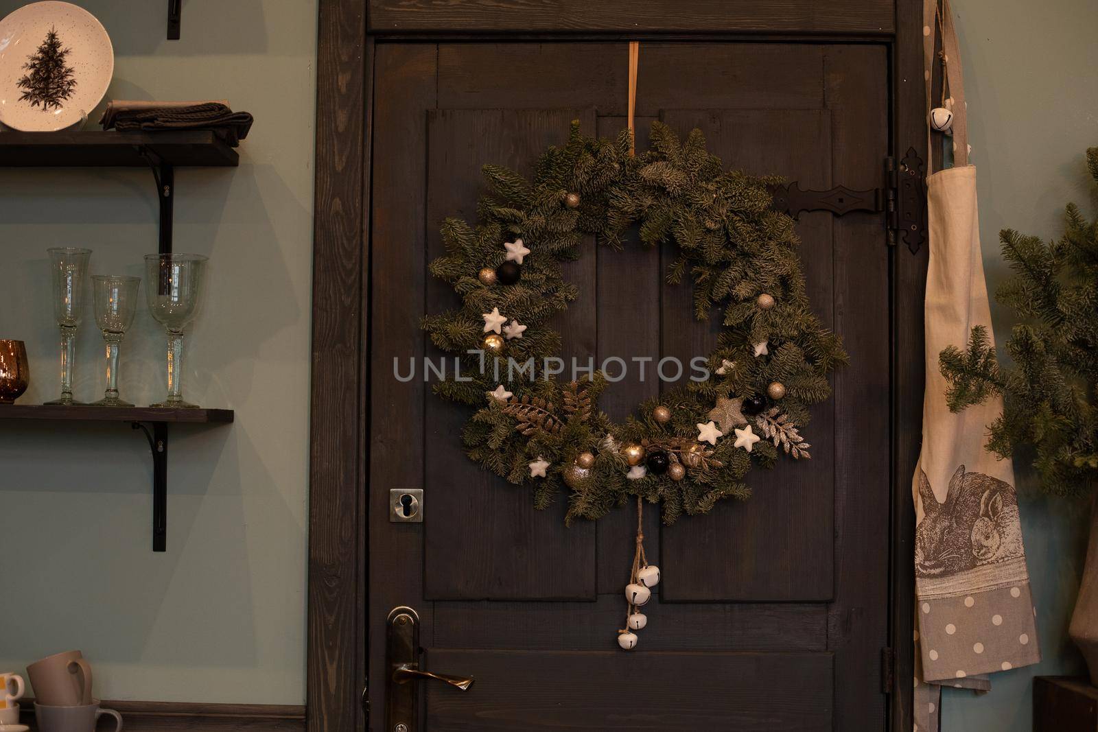 Close-up of fir tree Christmas wreath with decorations hanging on dark brown wooden front door of a house. Decorated Christmas wreath on the front door.