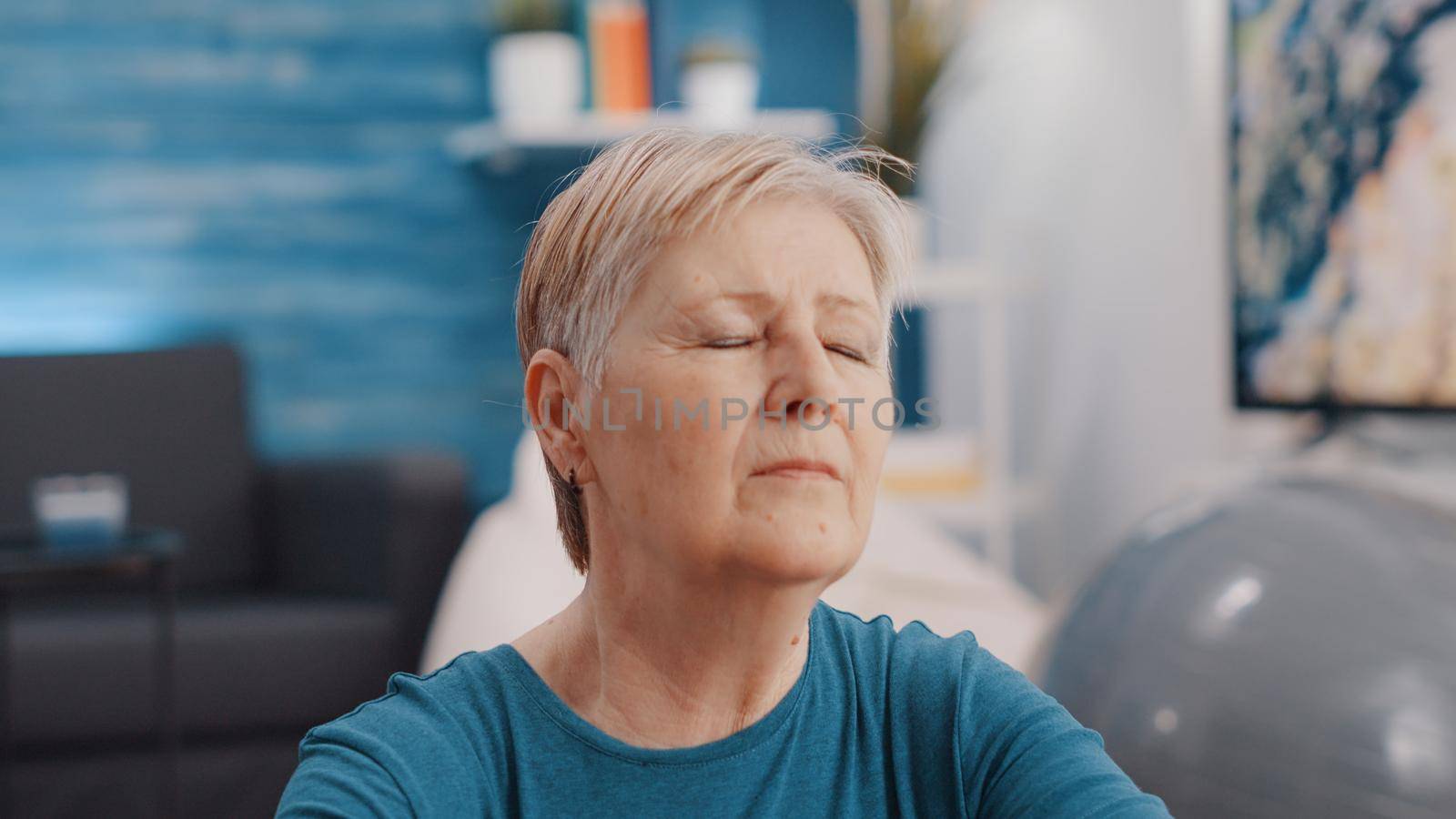 Close up of pensioner closing eyes and meditating to relax at home. Portrait of aged woman doing meditation for wellness and mindfulness. Calm retired person meditating and relaxing