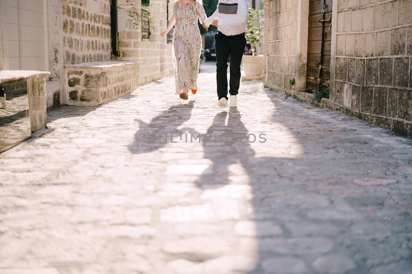 Man and woman run along the pavement of an ancient town. Close-up by Nadtochiy