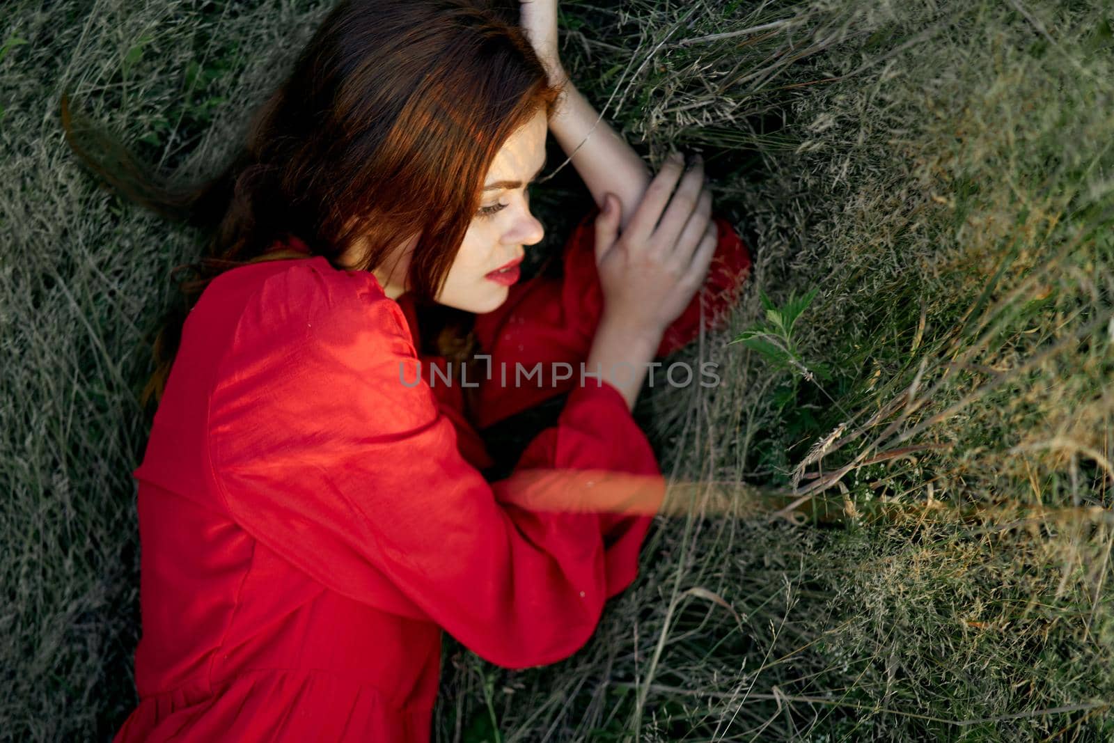 pretty woman in red dress lies on the grass posing top view. High quality photo