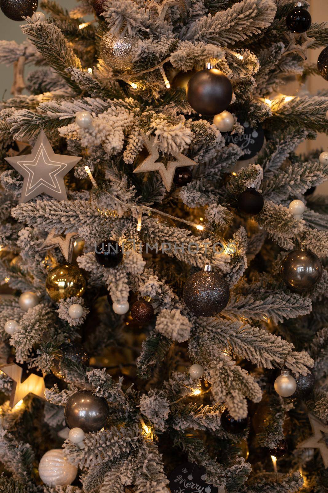 Close-up of beautiful snowed Christmas tree with garland and decorative balls and stars.