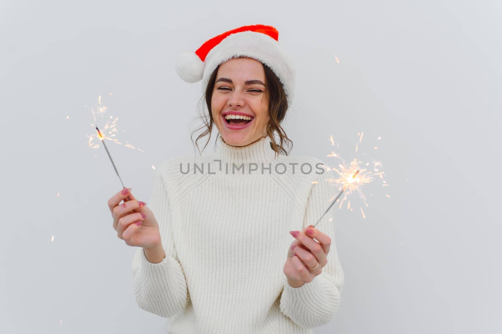 Lovely young woman in white sweater holds sparklers and laughs, smiles with a wide smile