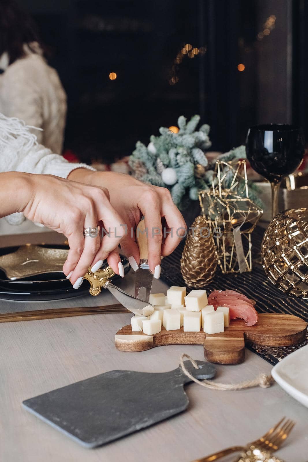 Cropped photo of woman tasting cheese on a wooden board with Christmas decorations in the background
