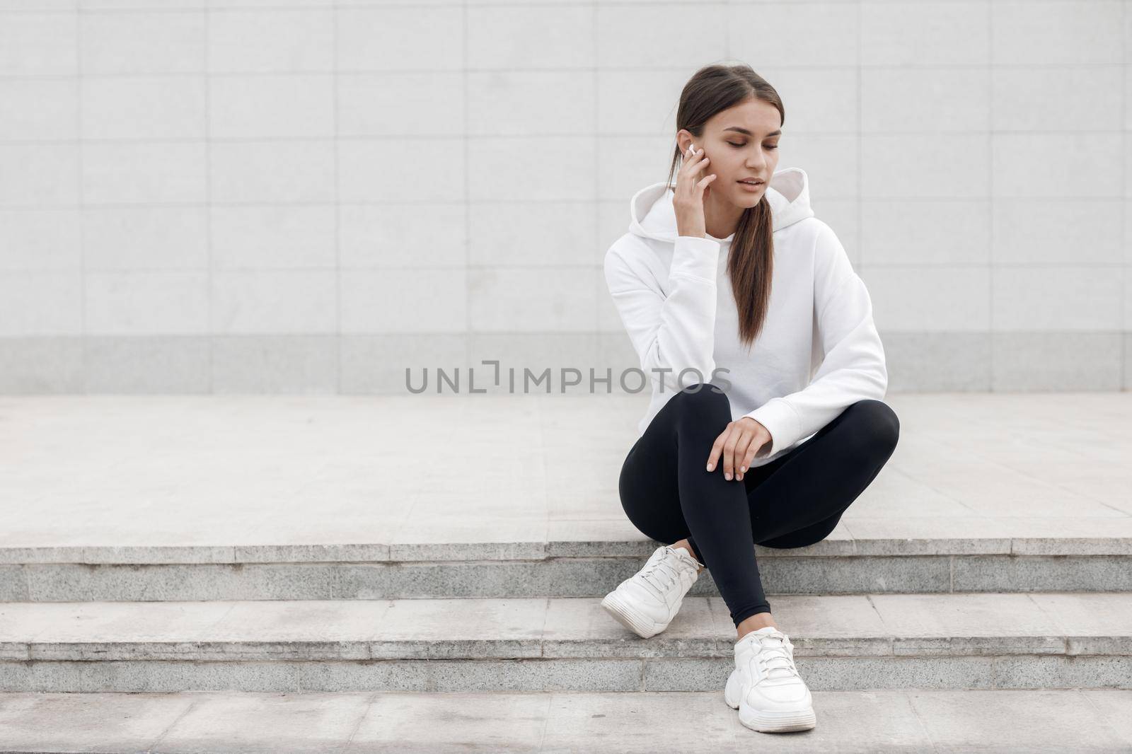 Young woman sitting after fitness outdoor with earphones by splash