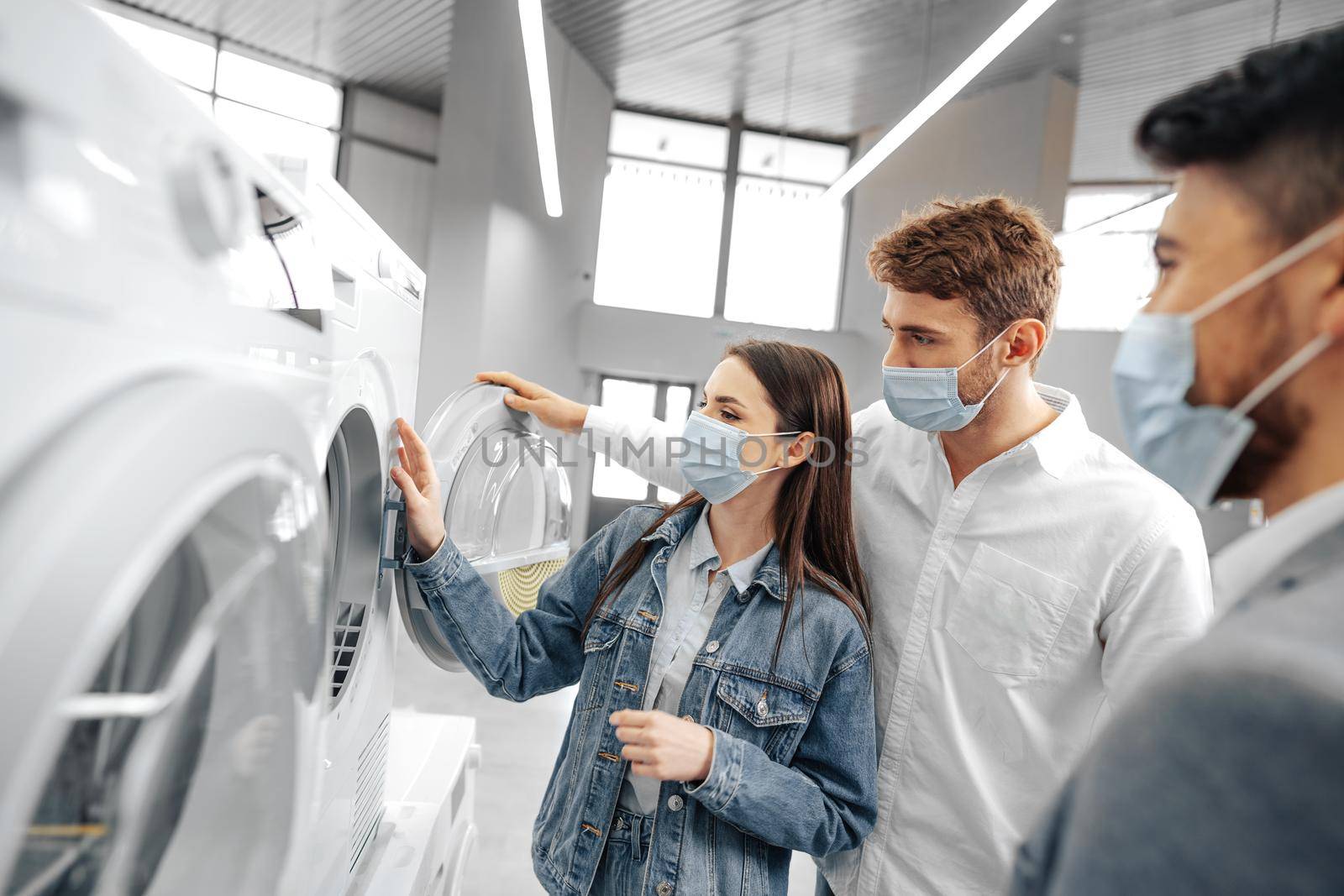 Salesman in hypermarket wearing medical mask demonstrates his clients a new washing machine, close up