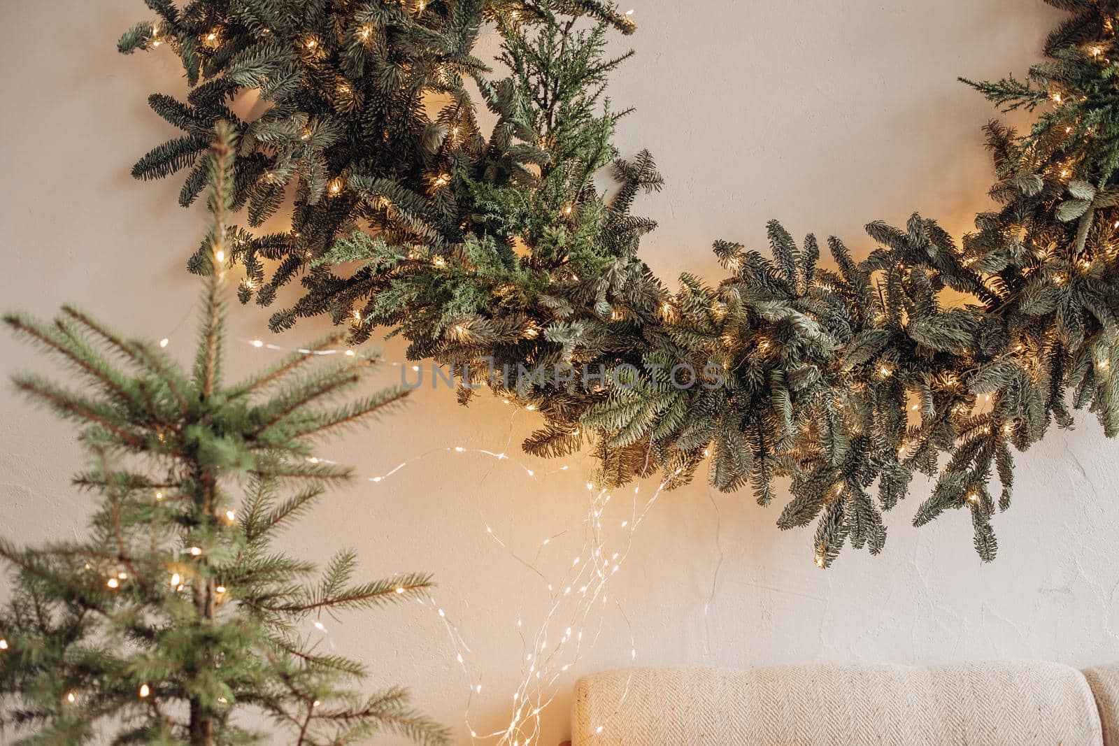 View over decorated artificial fireplace with decorations inside. Handmade paper stars, candles inside. Beautiful coniferous wreath on the top of fireplace. Decorative round mirror over the fireplace.