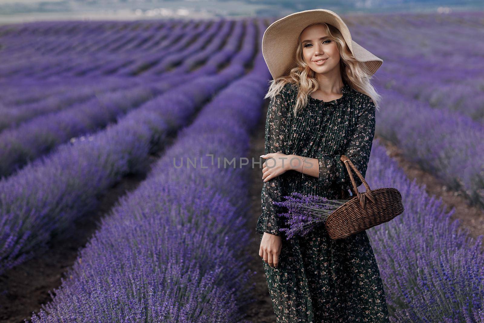 Fashion portrait of a pretty young woman in lavender field in hat with bag by splash