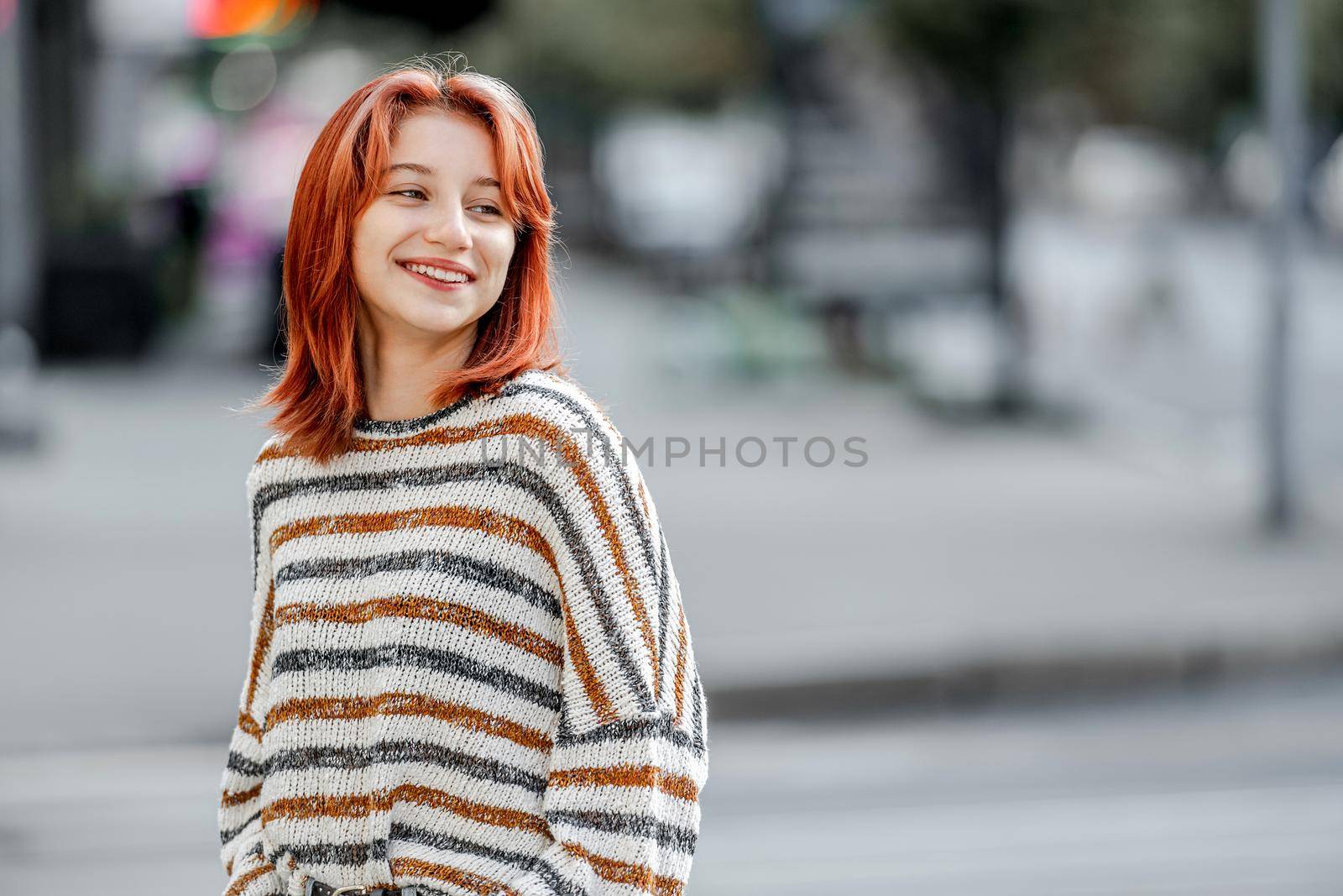 Stylish girl in casual trendy clothes walking at street and smiling. Urban portrait of pretty female teenager with bright hair