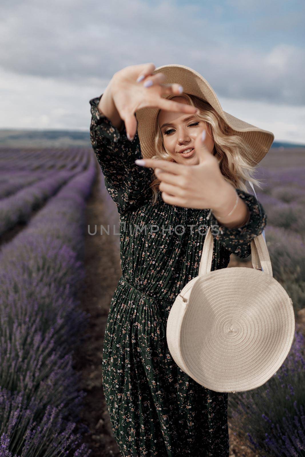 Fashion portrait of a pretty young woman in lavender field in hat with bag by splash