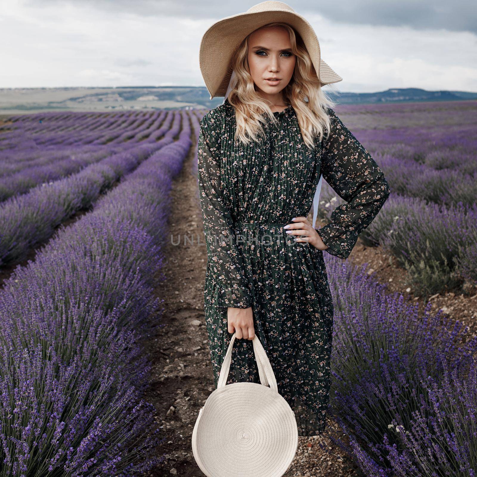 Fashion portrait of a pretty young woman in lavender field in hat with bag by splash