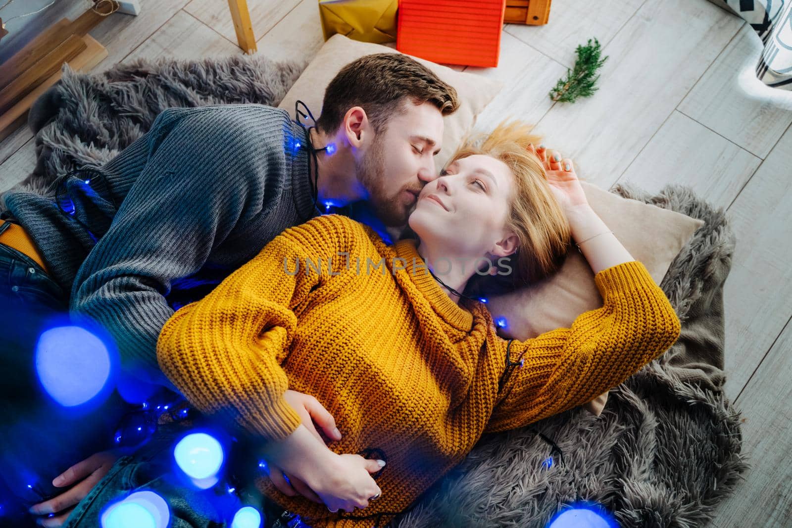 Beautiful and happy couple lies on a gray fluffy bedspread in a Christmas blue garland.