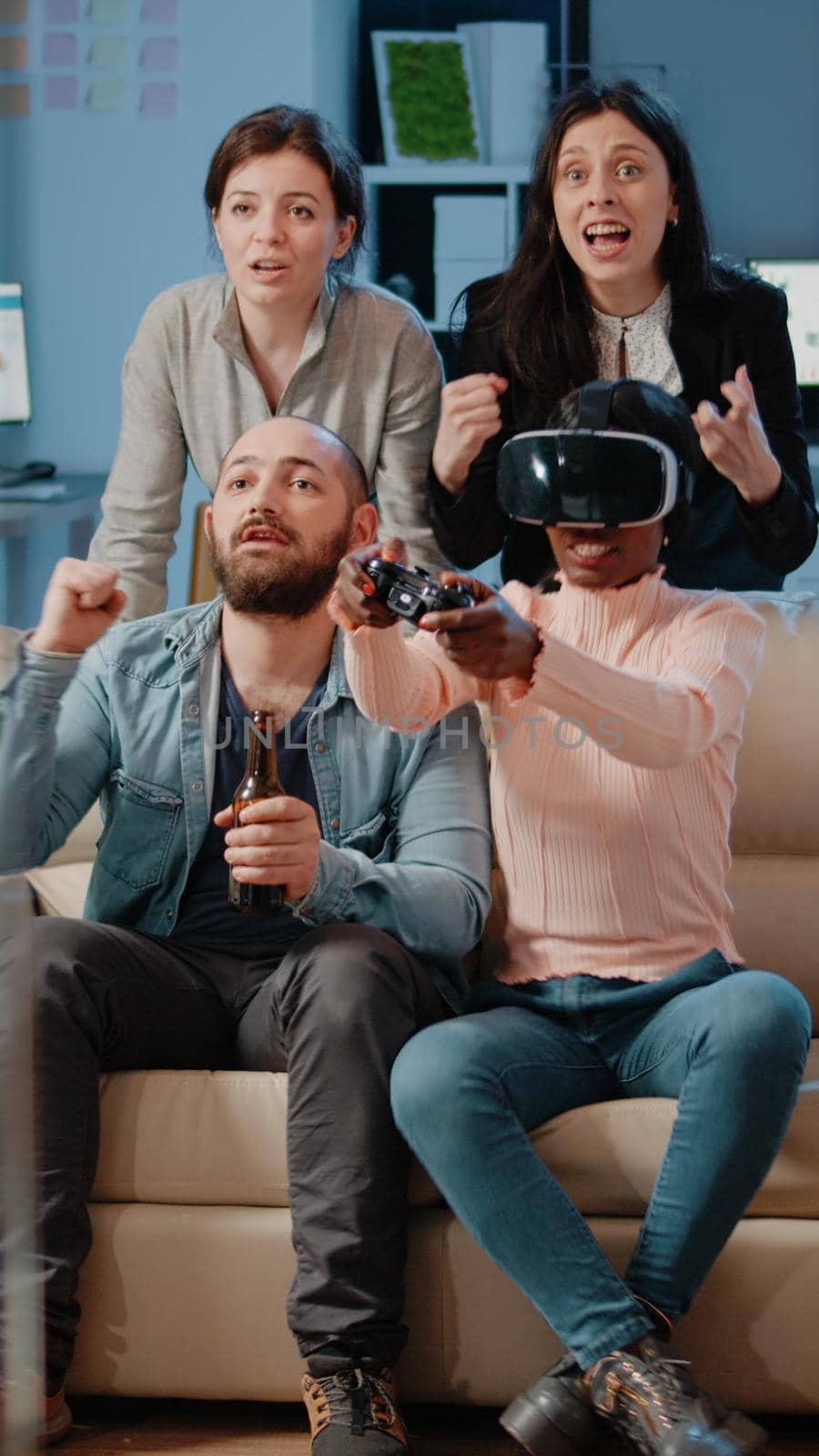 Multi ethnic people cheering while woman winning game with vr glasses and controller on tv console. Workmates enjoying video games with joystick to have fun with activity after work