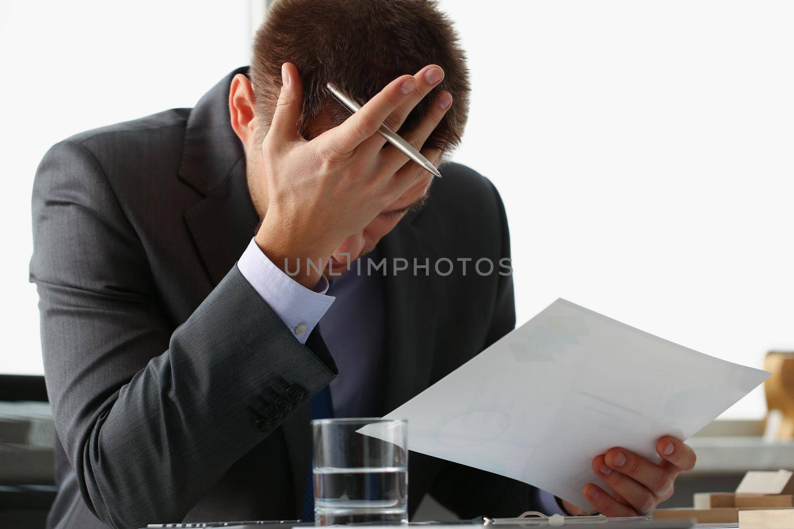 Close-up of adult man businessman hold paper sheet in hand and close face with palm. Wrong financial calculations led to failure. Business strategy concept