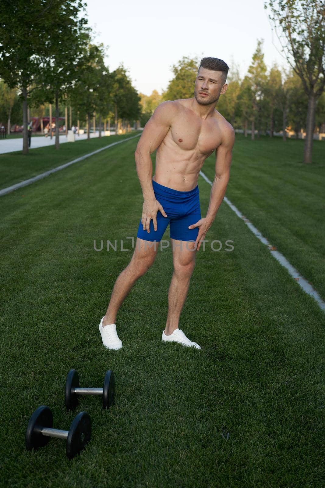 Muscled man in the park training with dumbbells. High quality photo