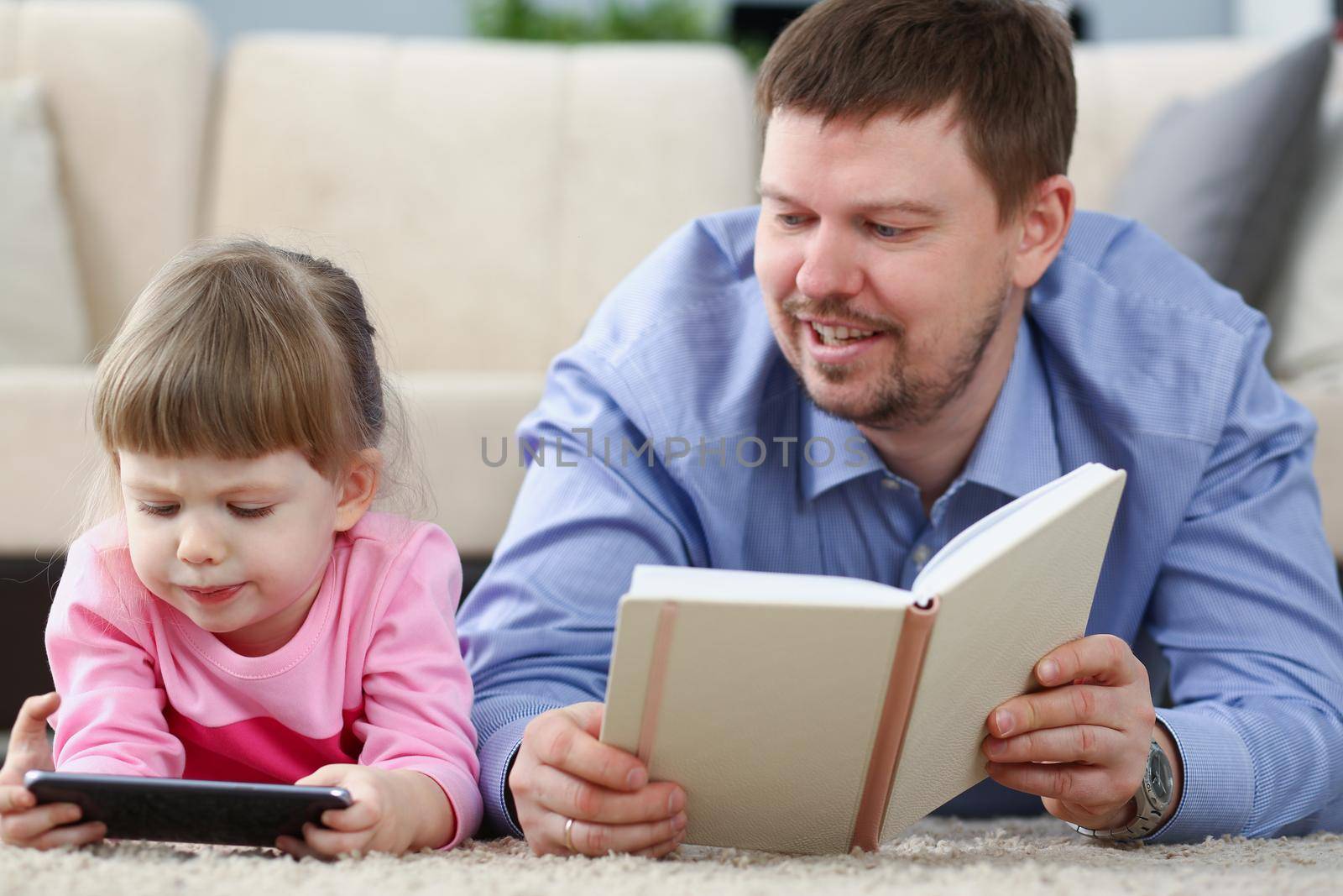 Portrait of father reading book to daughter while child stare at smartphone. Quality time with kid on holiday. Childhood, parenthood, addiction concept