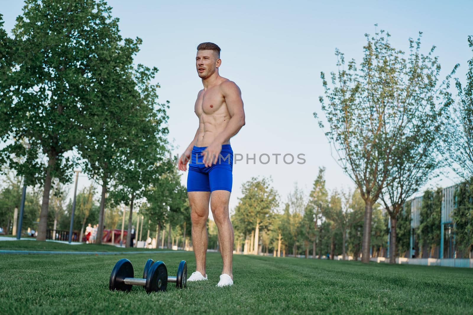 Muscled man in the park training with dumbbells. High quality photo