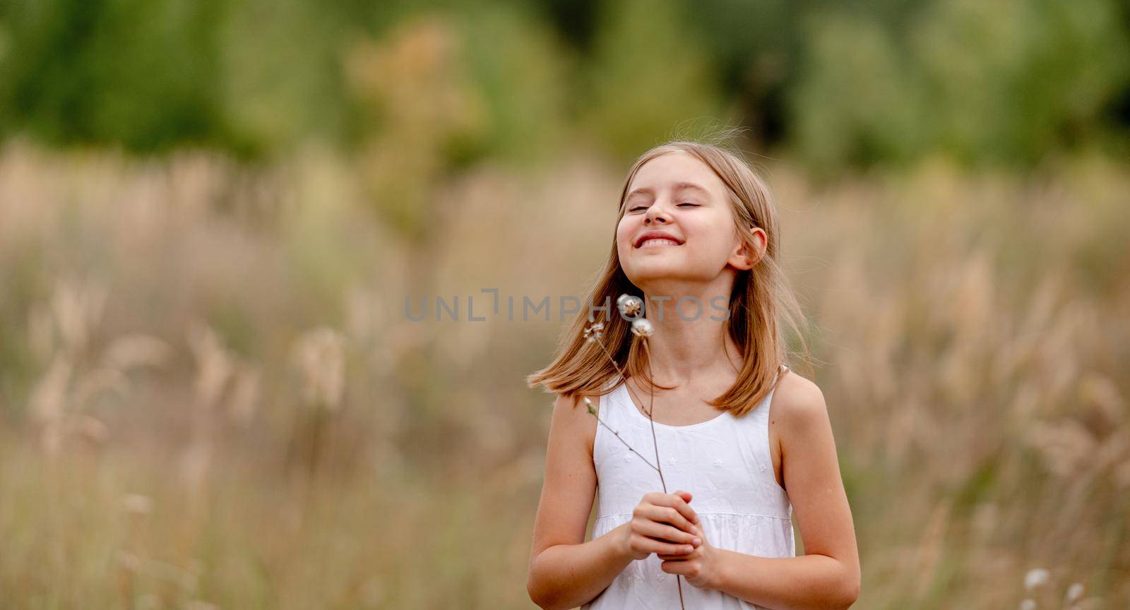 Preteen girl with flower in the field smiling and looking at camera. Pretty child kid enjoying the nature