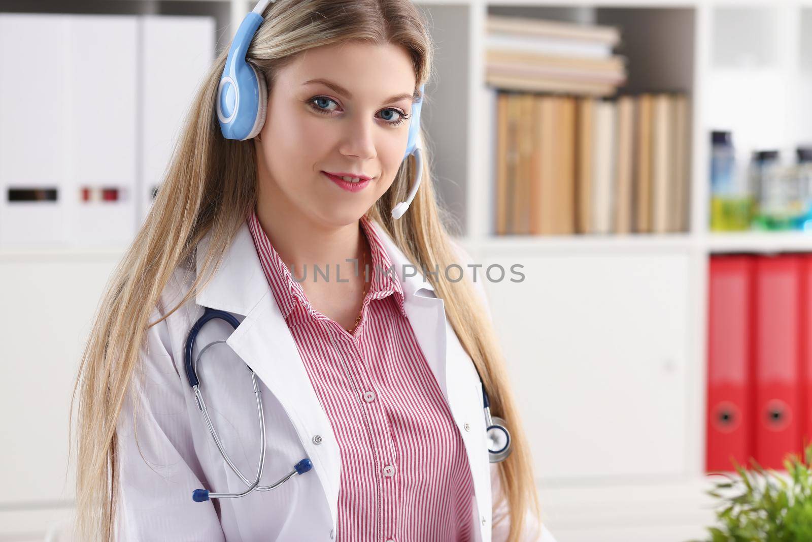 Portrait of pretty female blonde doctor talking to patient over wireless headset advises medical problem. Remote education, internship, callcenter concept