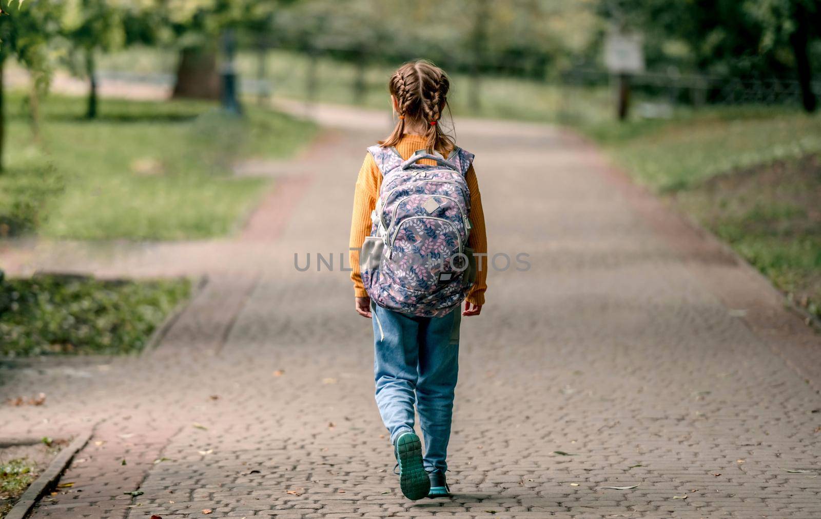 Preteen school girl with backpack walking in the park portrait from back. Carefree child kid at autumn outdoors