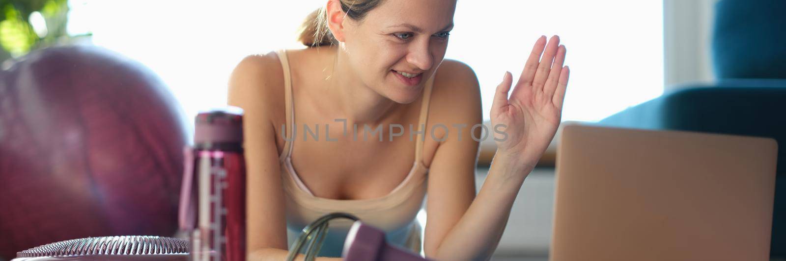 Smiling woman greets fitness trainer through laptop monitor. Introduction of sports blog remotely concept