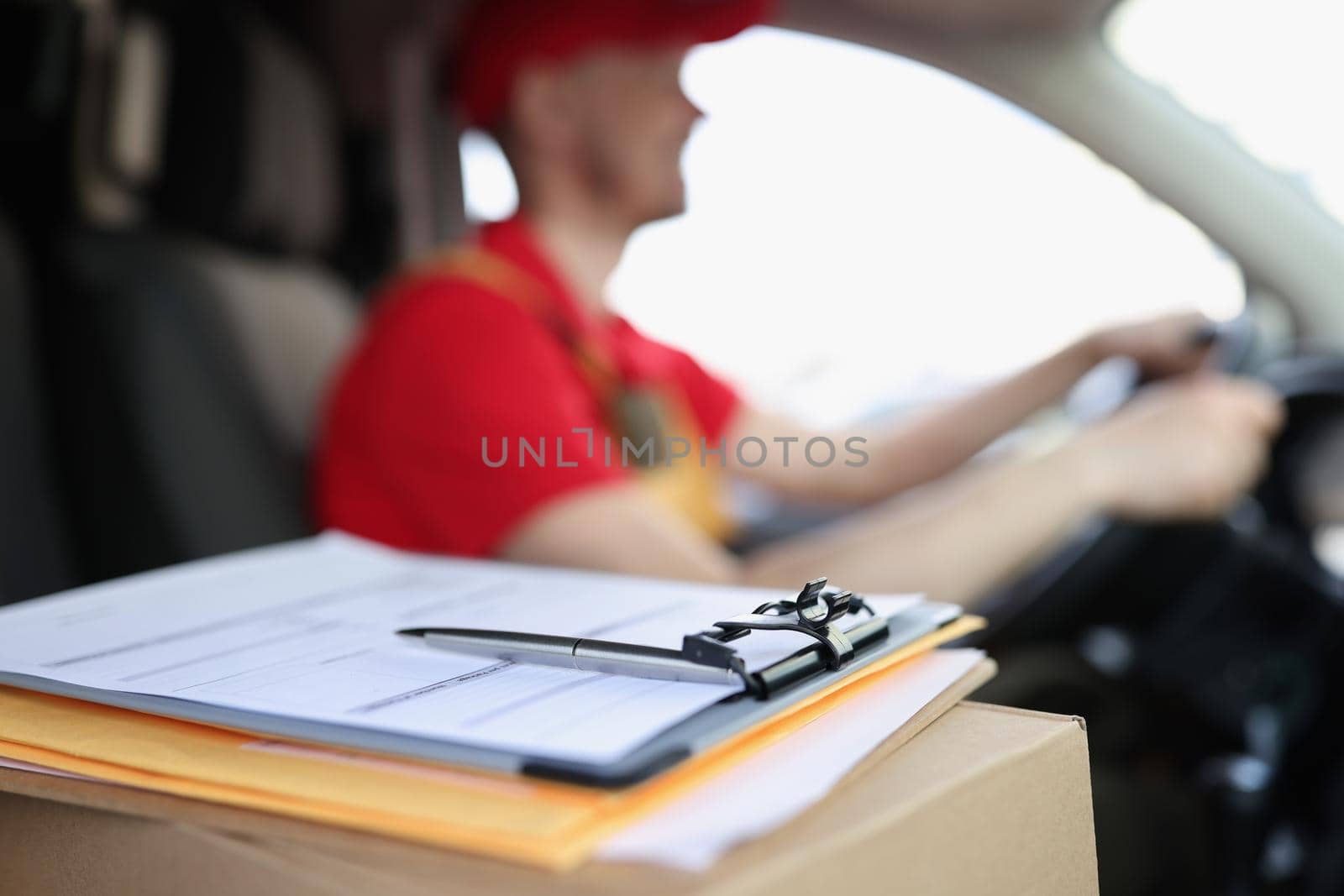 Close-up of docs on box and smiling courier deliver packages to people on car. Worker in special red uniform. Delivery service, shipping, transfer concept