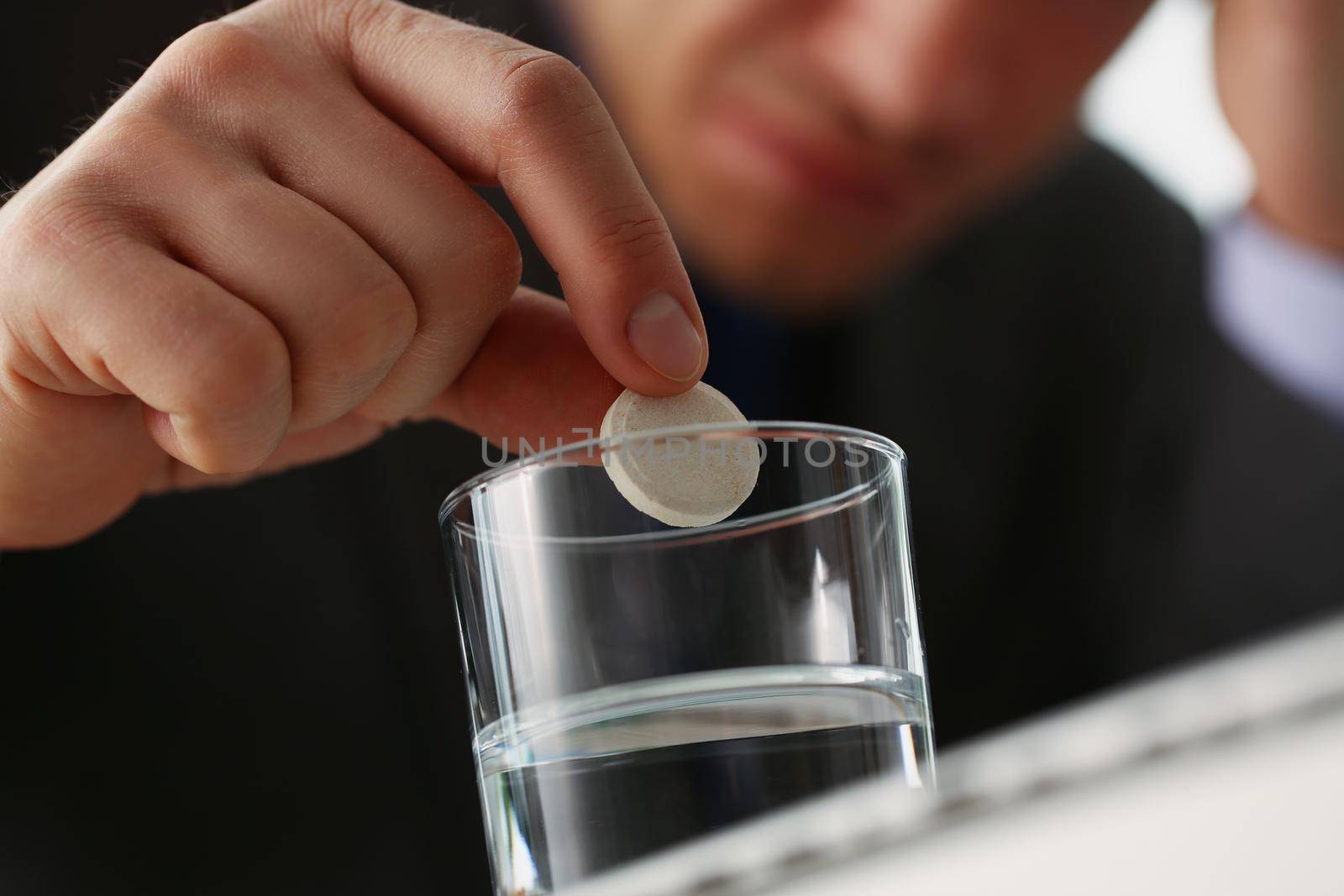 Close-up of tired man put tablet in glass with water to stop headache because of big workload. Aspirin medication to relief pain. Medicine, remedy concept