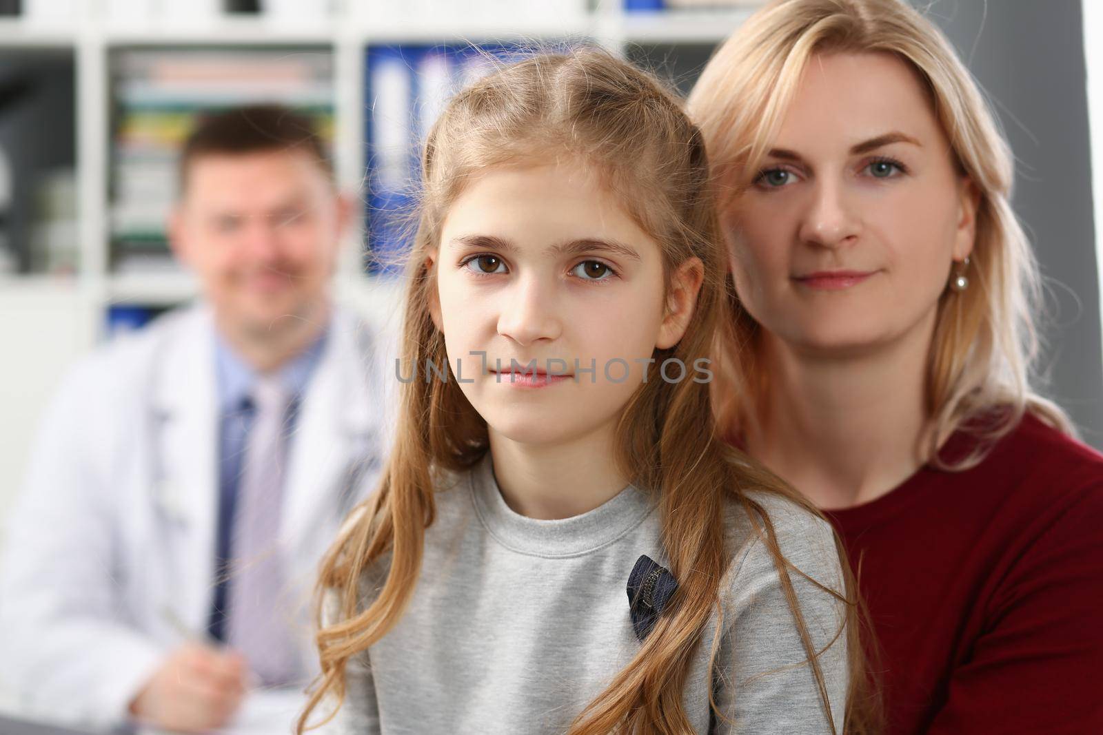 Portrait of mother and daughter on doctors appointment, medical worker smile behind. Need for qualified advice and professional help. Family doctor concept