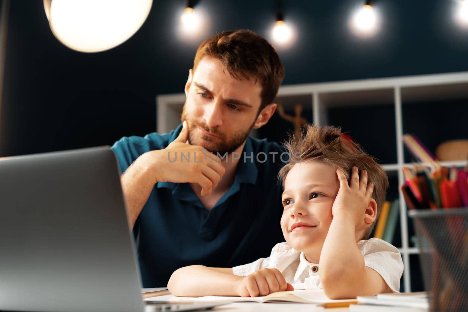 Young boy sitting with his father at the table and using laptop for study