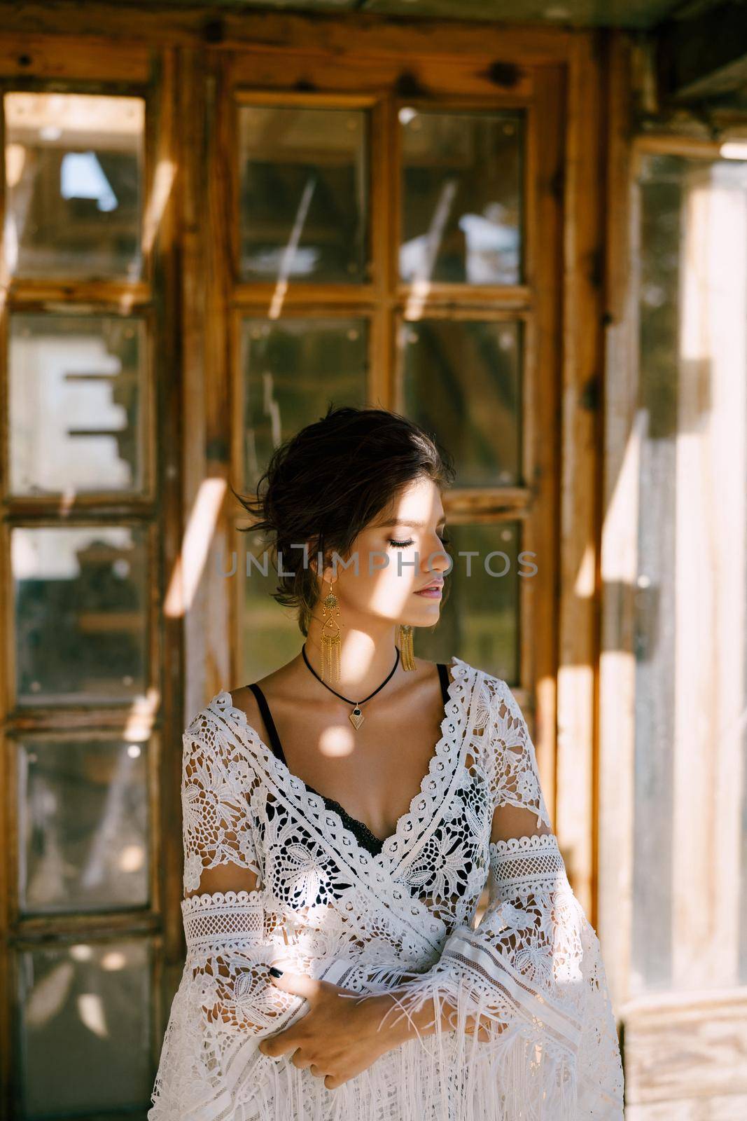 Woman in a white lace cape sits near an antique wooden door. Portrait by Nadtochiy