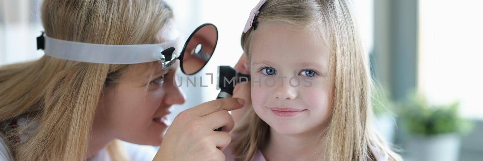 ENT doctor looks at little girl's ears with otoscope. Hearing test in children concept