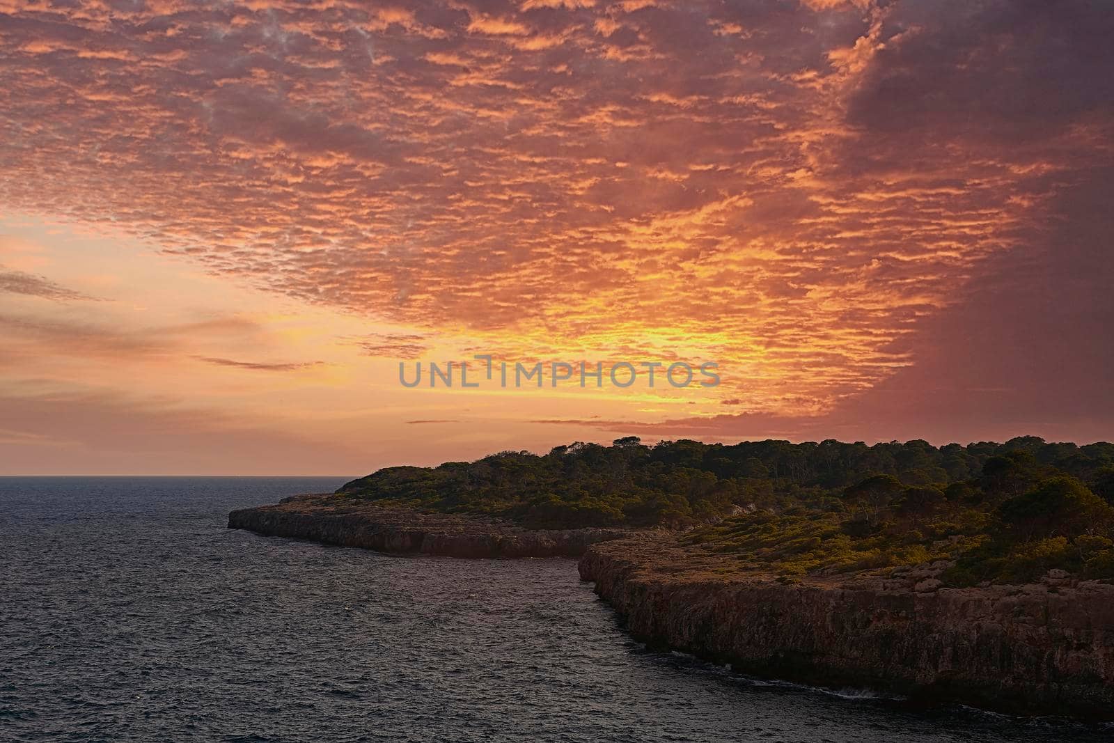 Sunset or sunrise on the coast with cliffs. Orange sky with clouds, no people