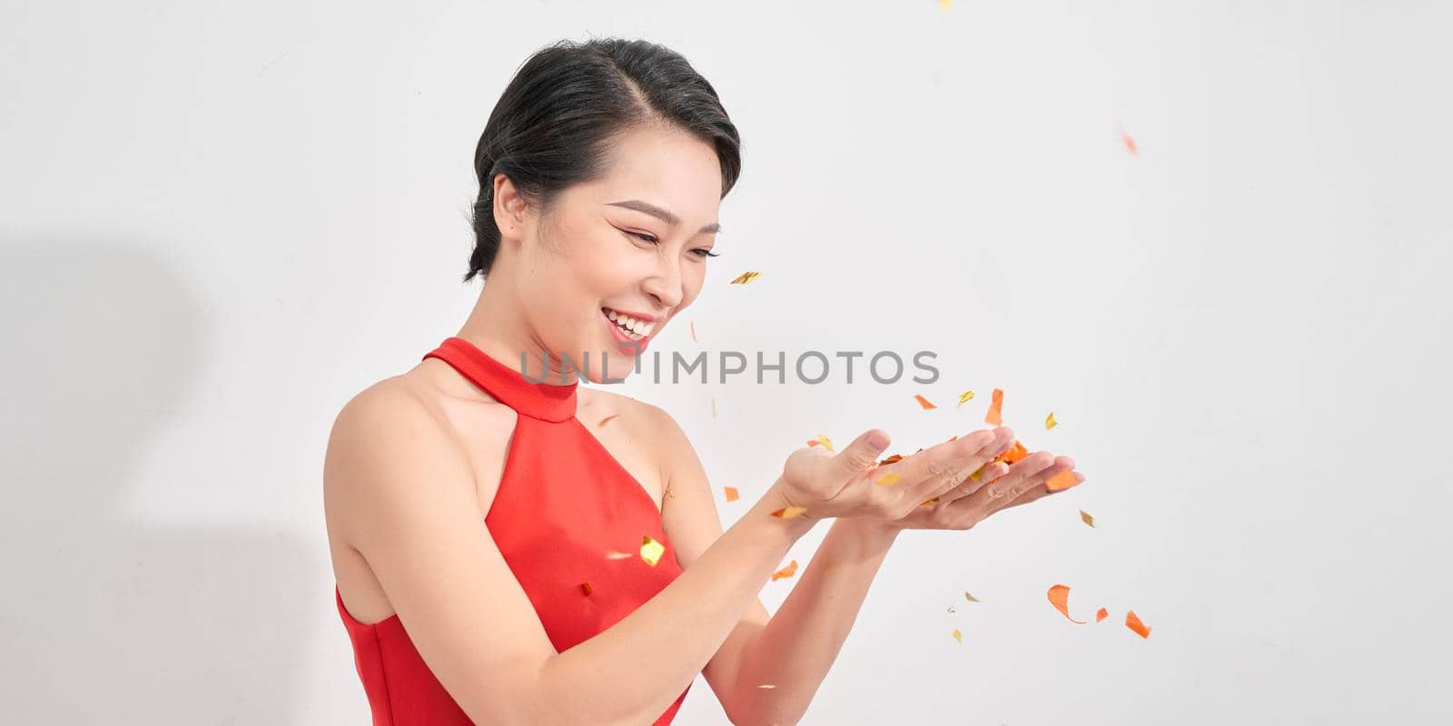 pretty woman blows confetti in the air wearing red dress isolated over white by makidotvn
