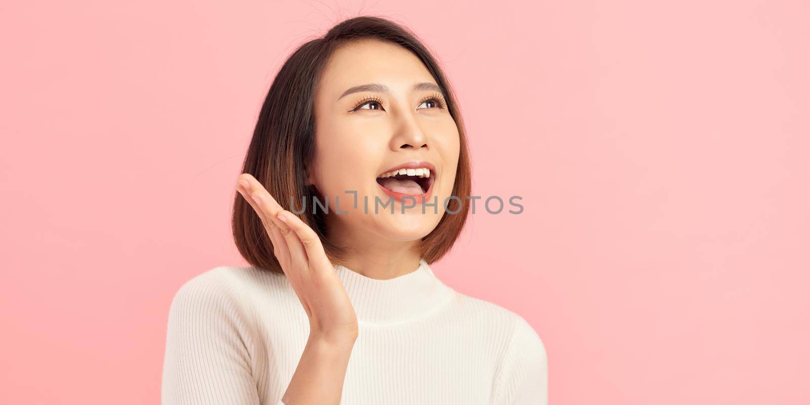 Energetic loud cute beautiful female opening mouth widely, putting hands to mouth, shouting standing isolated over pink background  by makidotvn