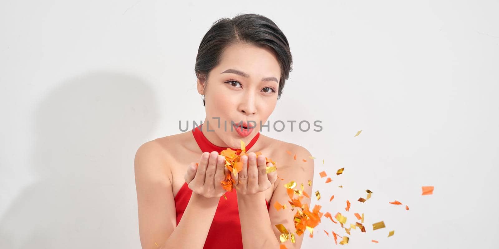 pretty woman blows confetti in the air wearing red dress isolated over white by makidotvn