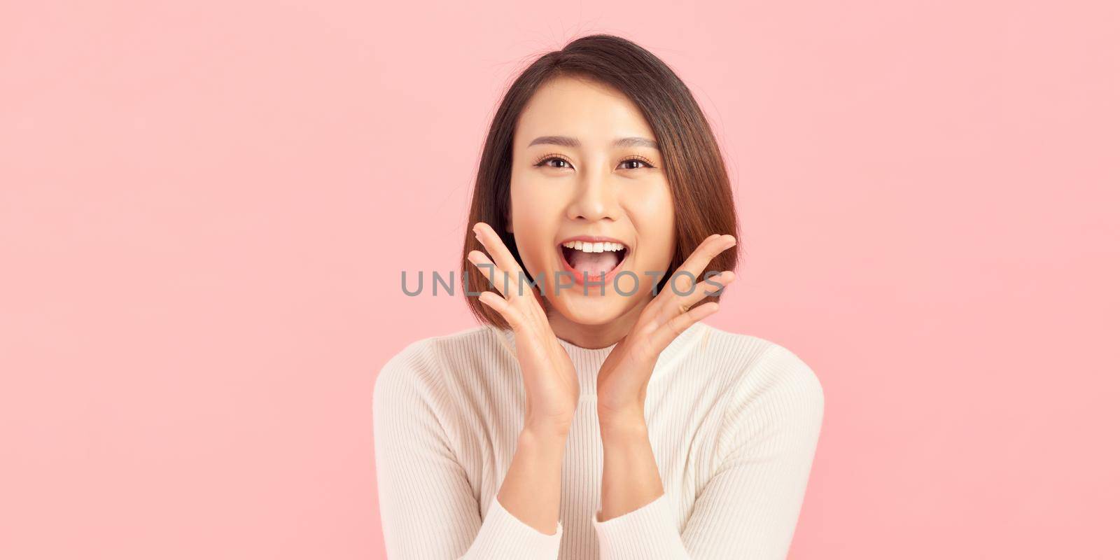 Scream and shout! Pretty young woman holding hands near opened mouth. Pink background.