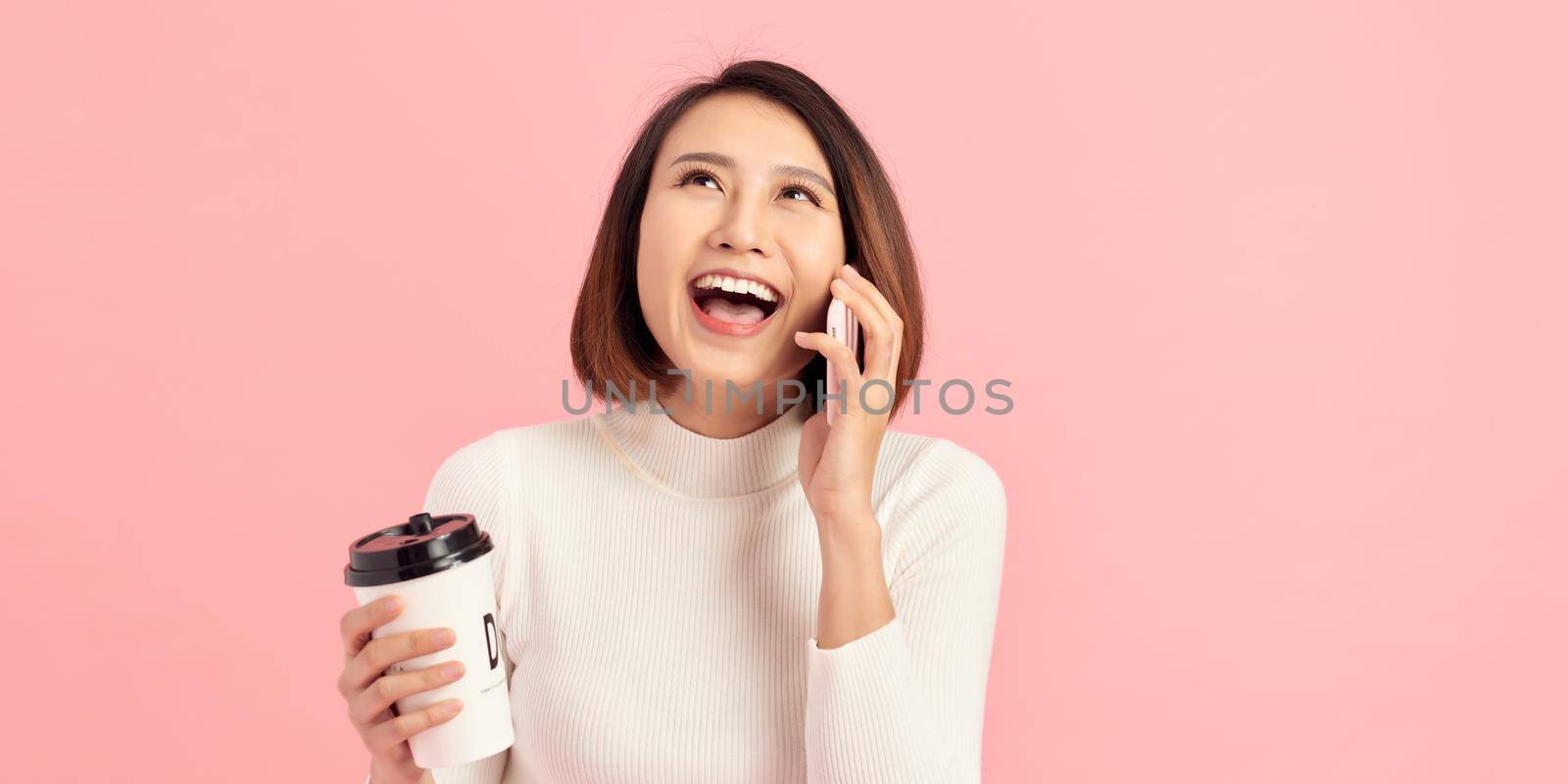 Young woman over isolated background holding coffee to take away and a mobile