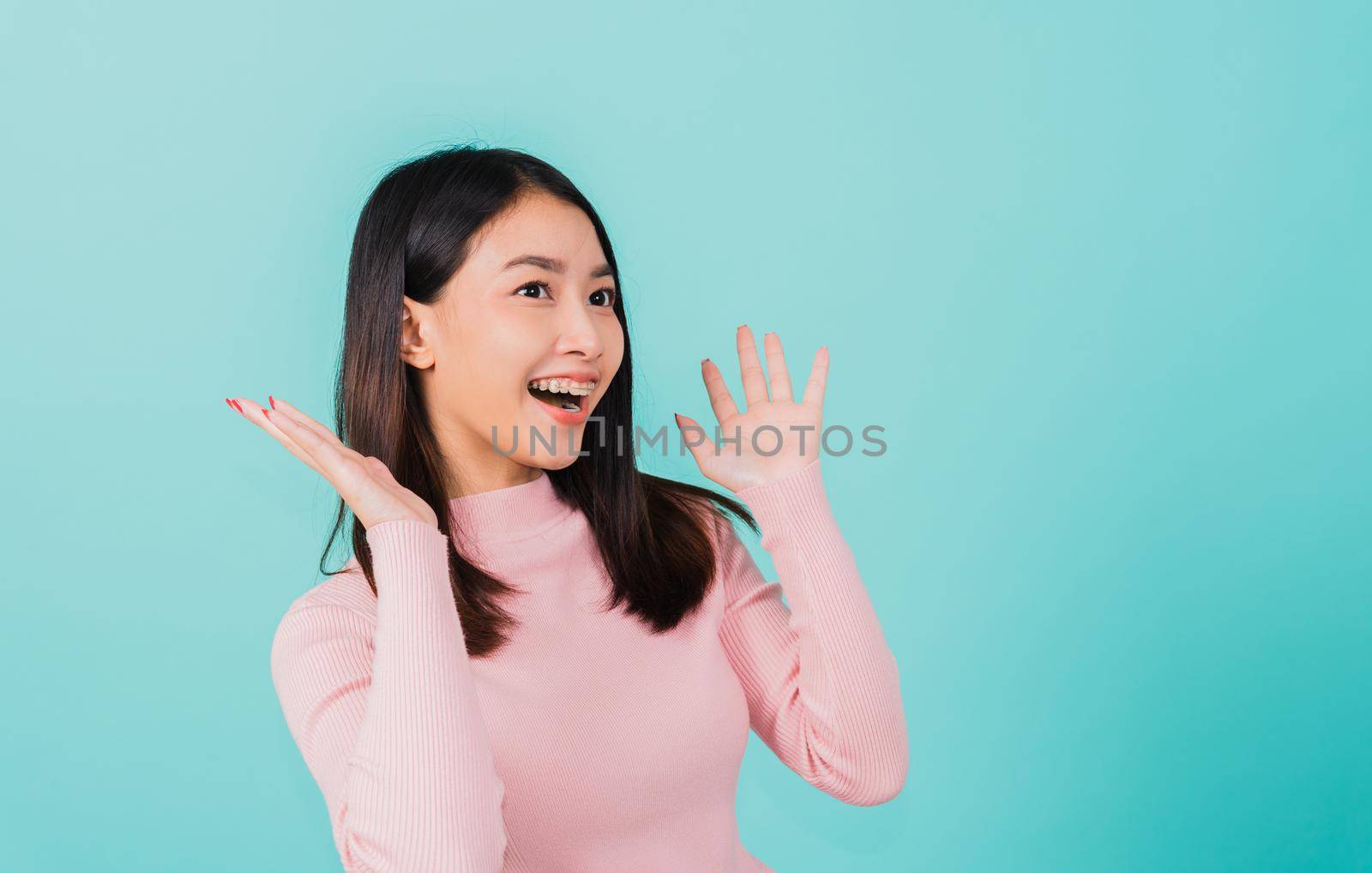 Happy young Asian beautiful woman smiling wear silicone orthodontic retainers on teeth surprised she is excited screaming and raise hand make gestures wow, studio shot isolated on blue background