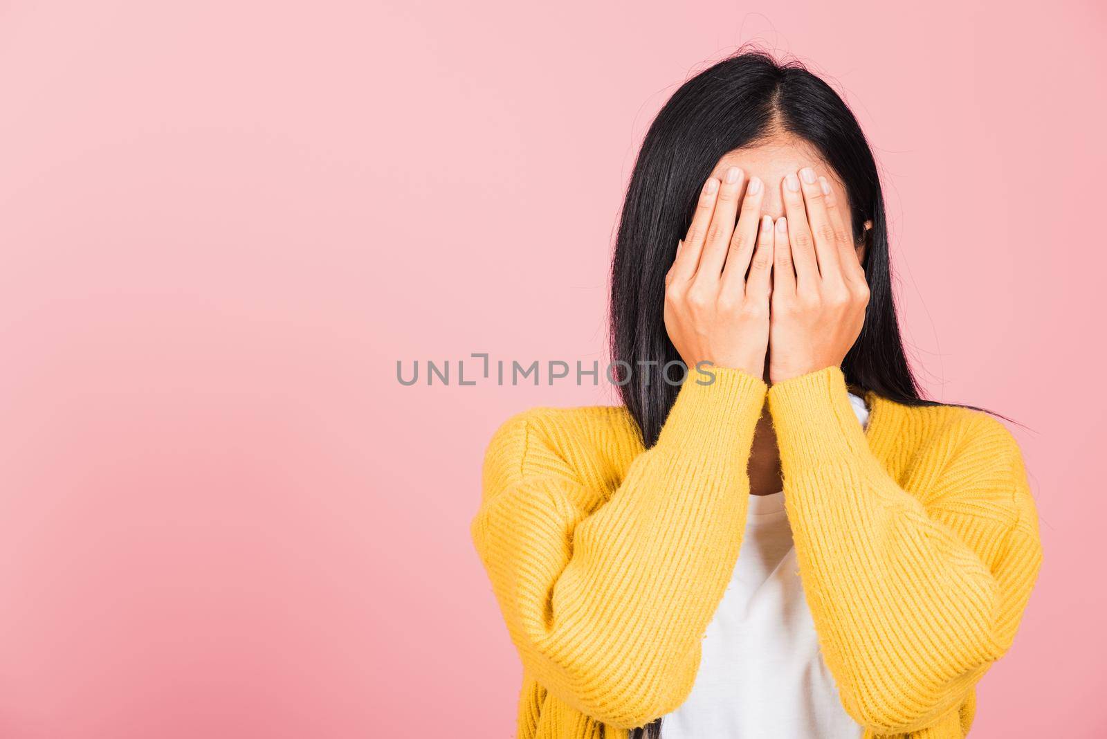 Asian portrait beautiful young woman in depressed bad mood her cry close face by hands because of being embarrassed studio shot isolated on pink background surprised and shocked with copy space