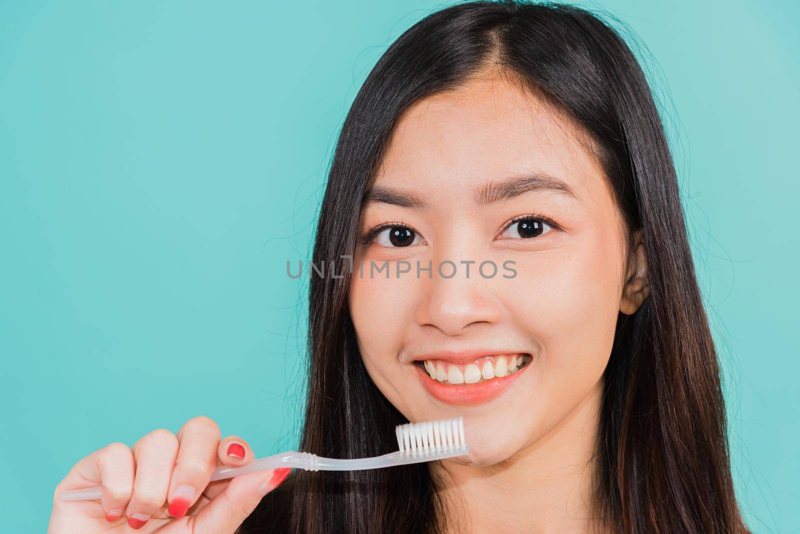 Asian beautiful young woman teen brushing teeth in the morning, portrait of happy Thai female confident smiling holding toothbrush, studio shot isolated on blue background, Dental health concept