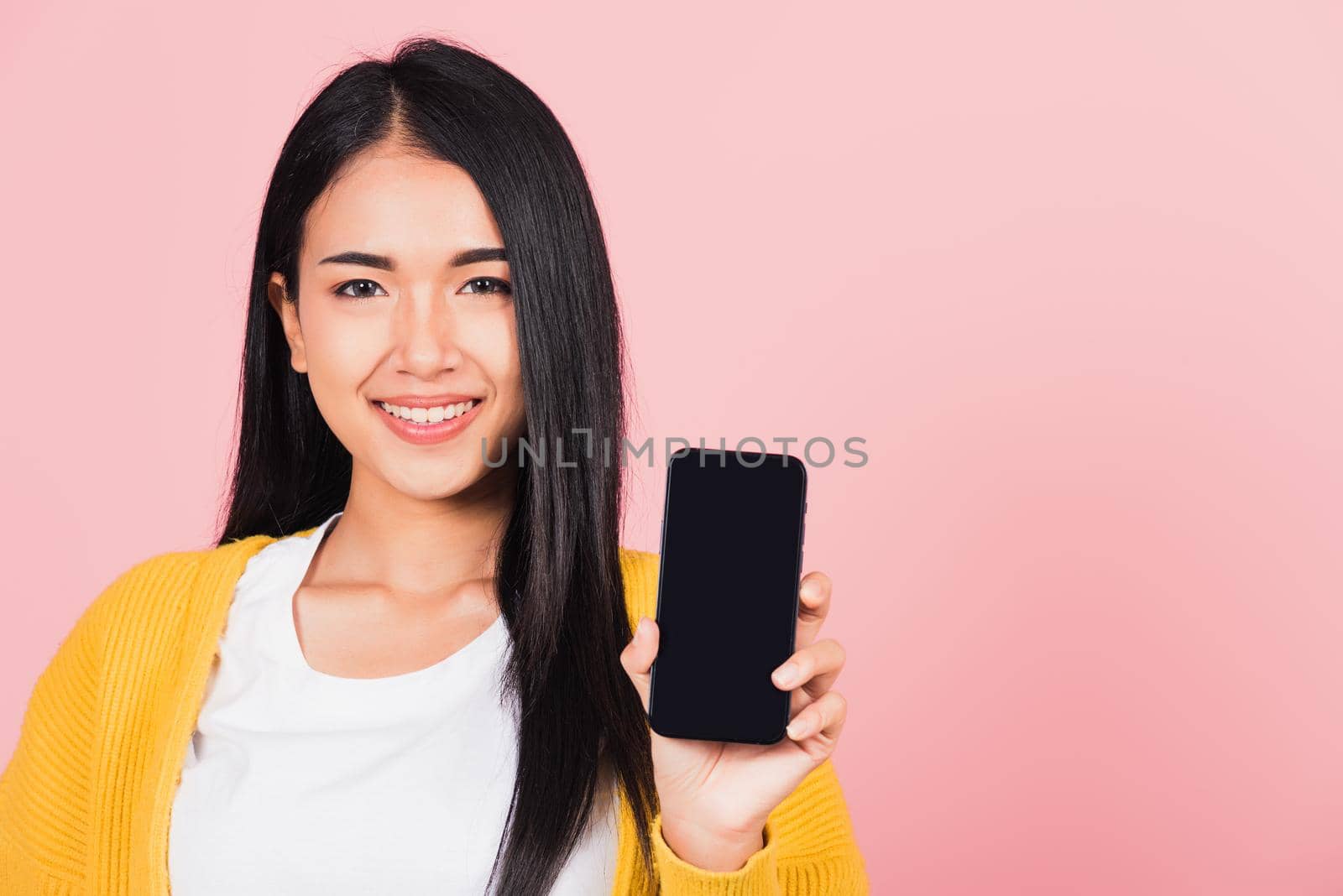 Happy Asian portrait beautiful cute young woman teen smiling excited  holding blank screen mobile phone studio shot isolated on pink background, Thai female show smartphone empty screen space
