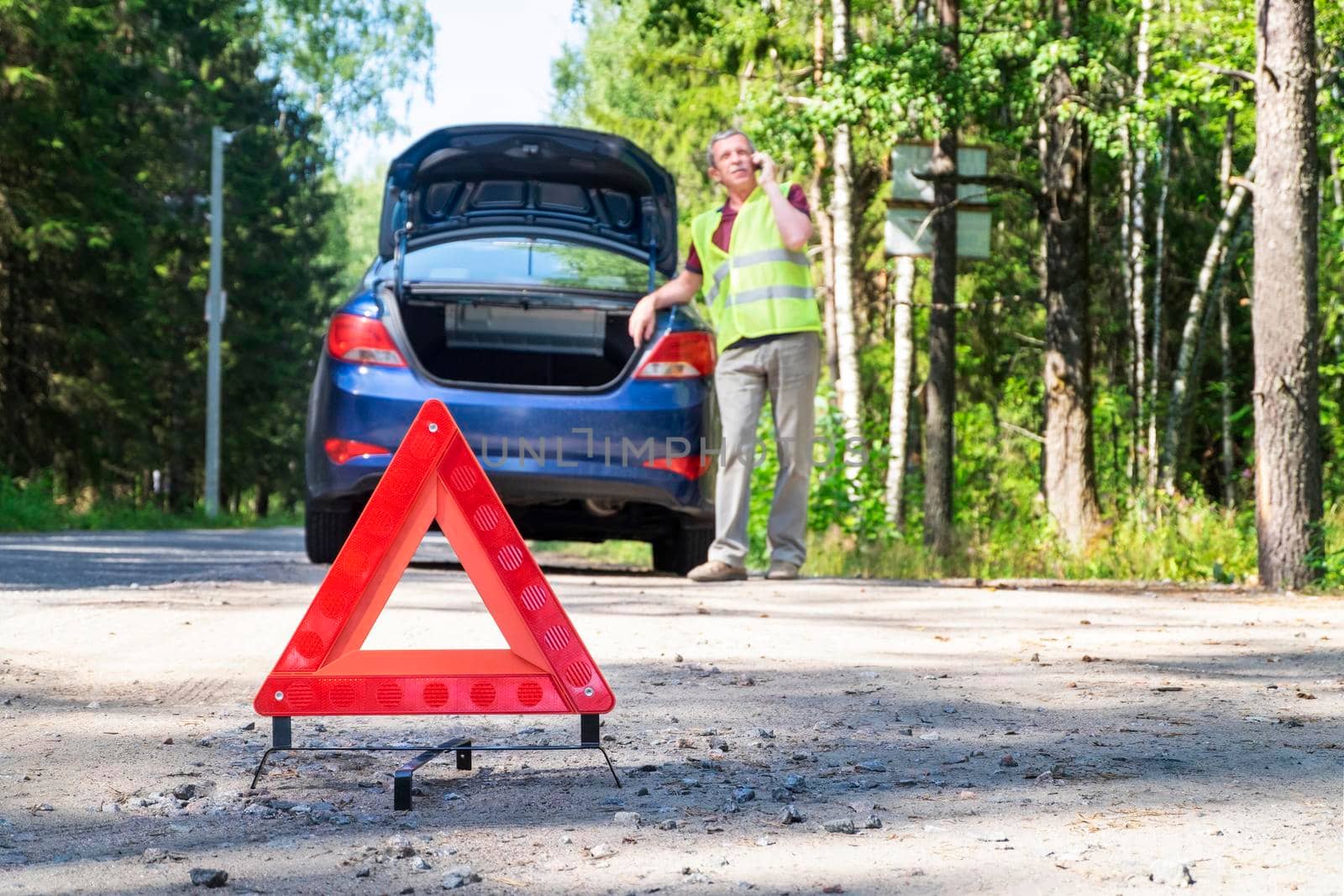Portable warning triangular sign on the side of rural road near a car by OlgaGubskaya