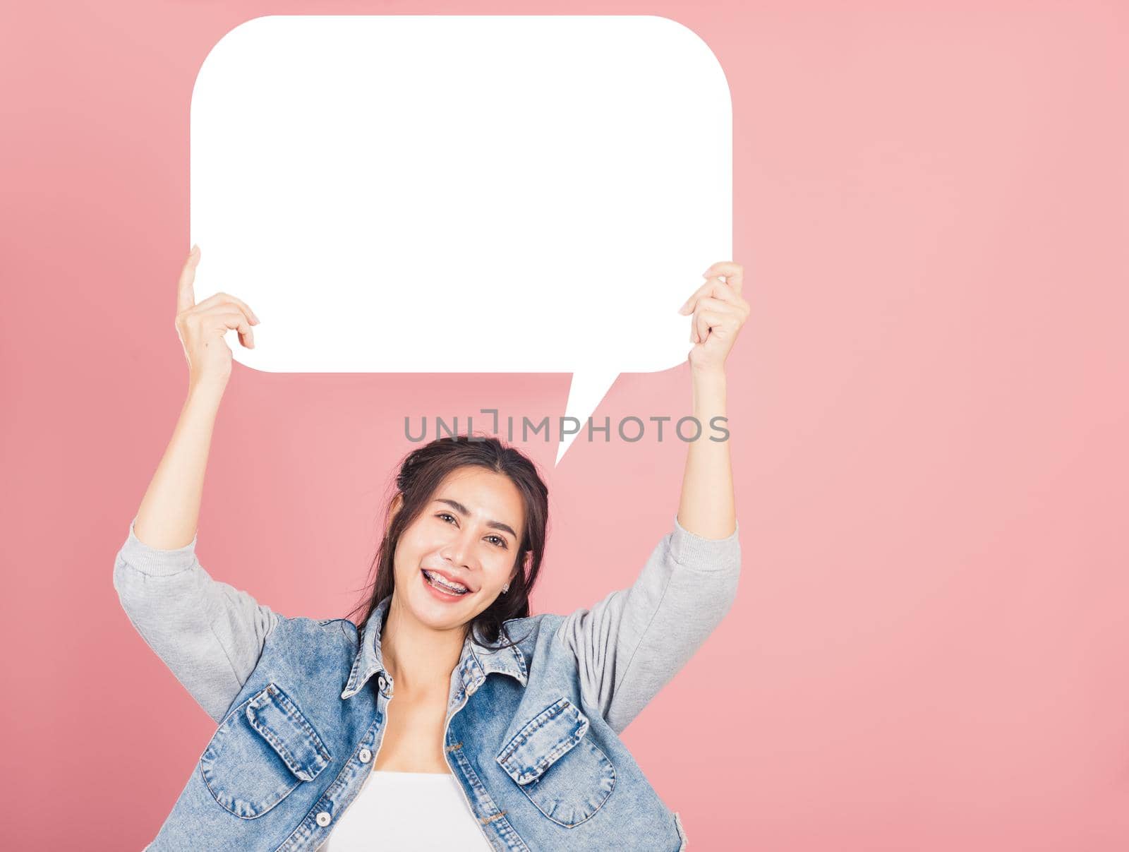 Happy Asian beautiful young woman smiling excited wear denims holding empty speech bubble sign, Portrait female posing show up for your idea looking at camera, studio shot isolated on pink background