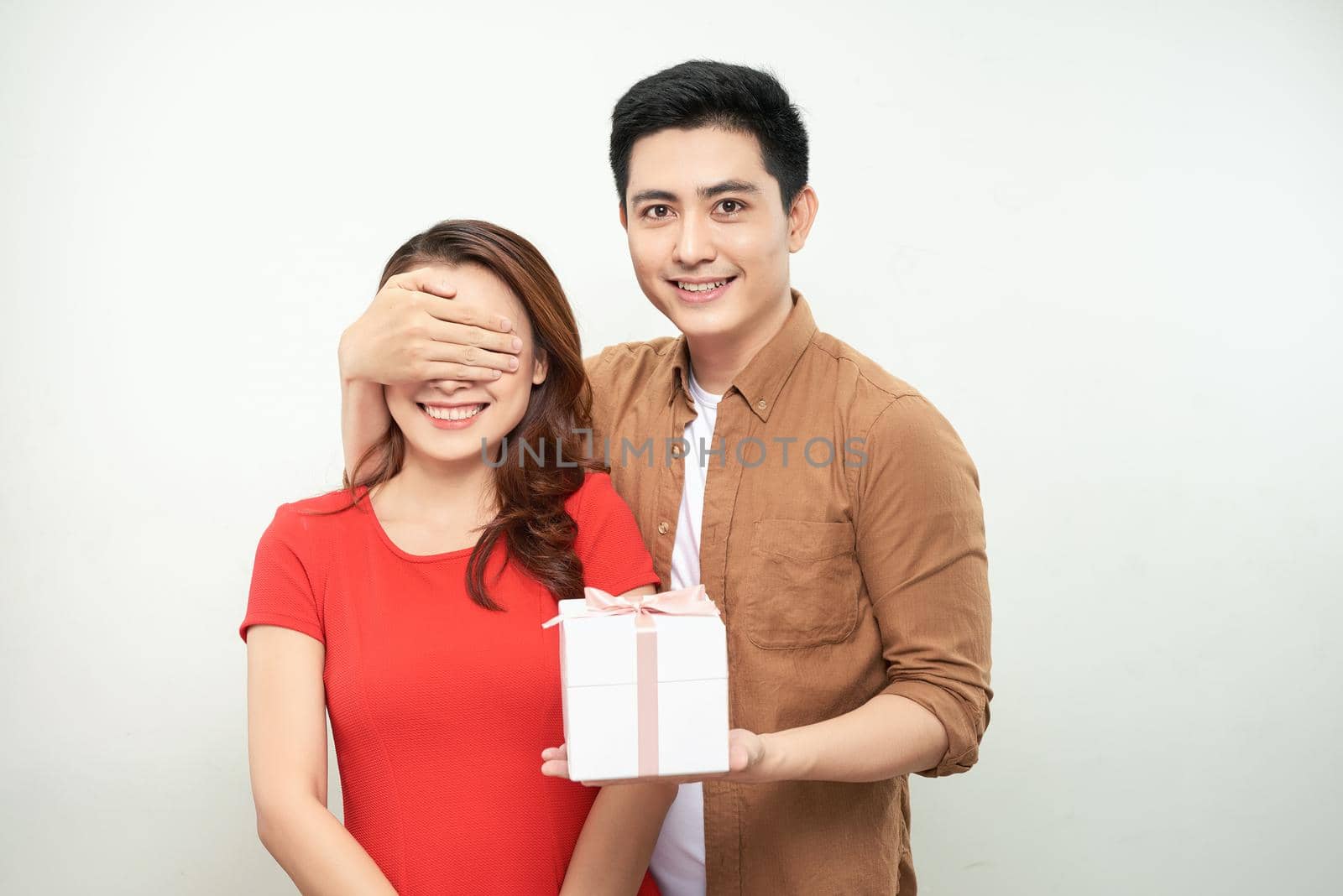 Happy Anniversary, Honey! Attractive asian Man Closing His Woman Eyes, holding gift for her, white background