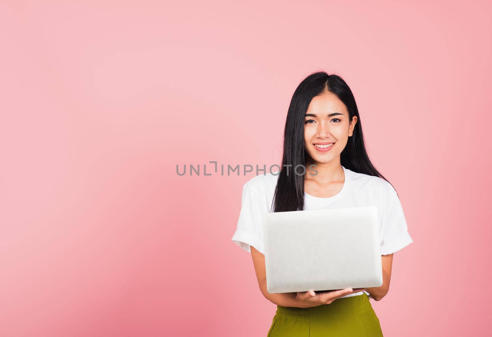 Portrait of happy Asian beautiful young woman confident smiling face holding using laptop computer looking to camera, studio shot isolated on pink background, with copy space
