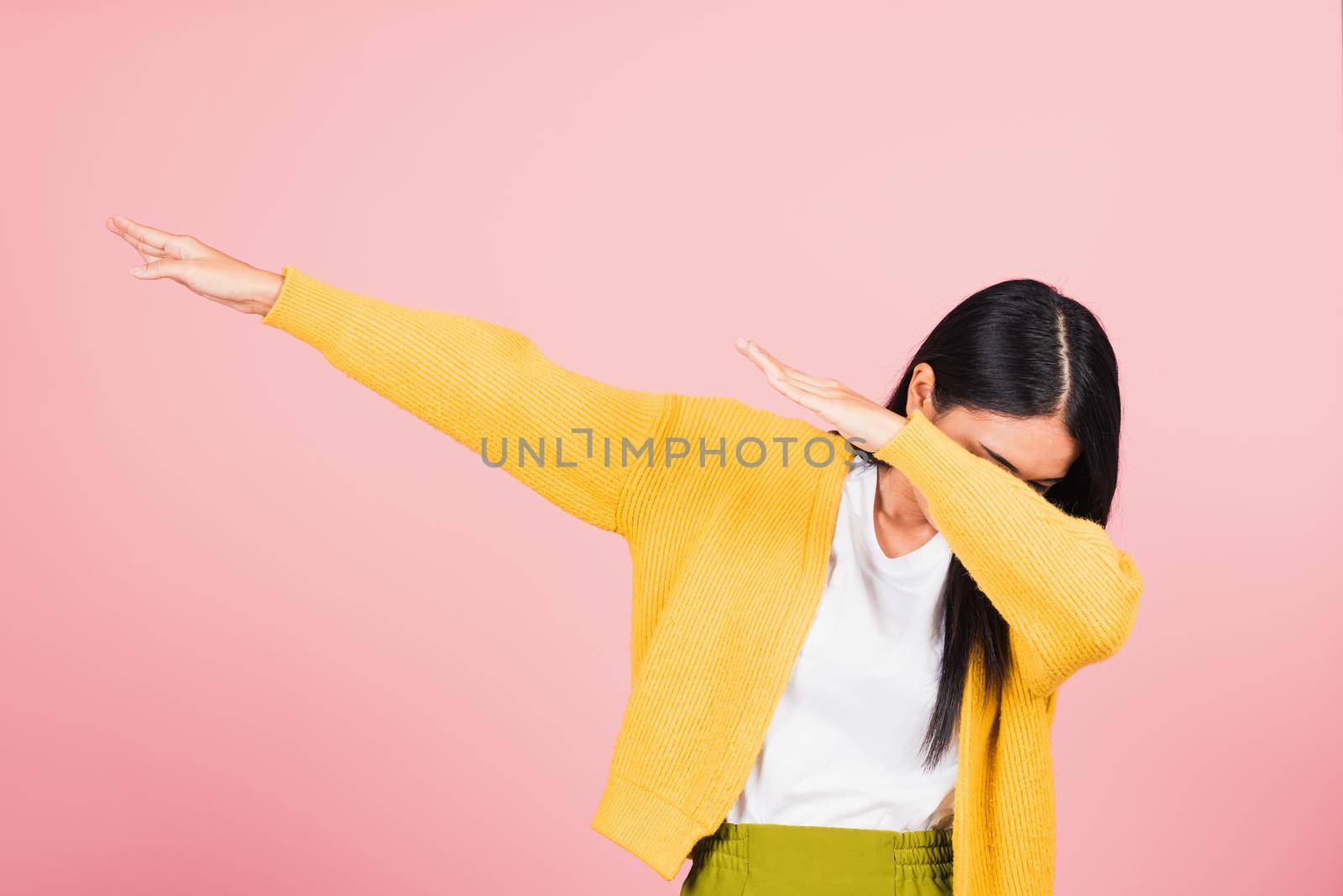 Asian happy portrait beautiful cute young woman teen smile standing move showing DAB dance against gesture raise hands arms covering  face isolated, studio shot on pink background with copy space