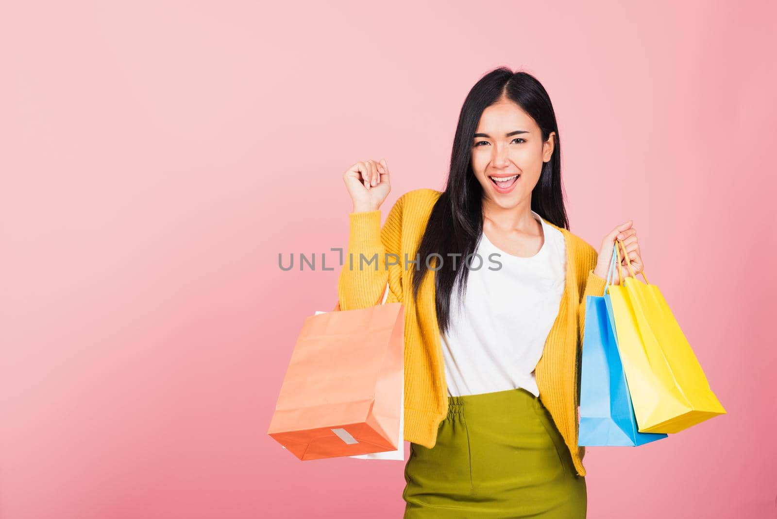 Portrait of Asian happy beautiful young woman teen shopper smiling standing excited holding online shopping bags colorful multicolor in summer, studio shot isolated on pink background with copy space