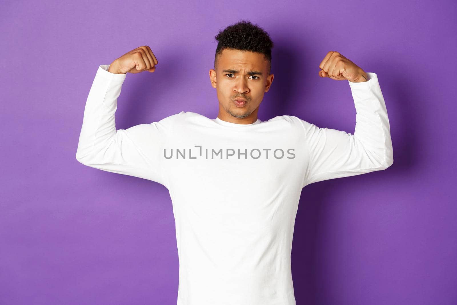 Image of confident african-american young guy, flexing biceps and trying to show-off, showing muscles after workout, standing over purple background, feeling strong by Benzoix