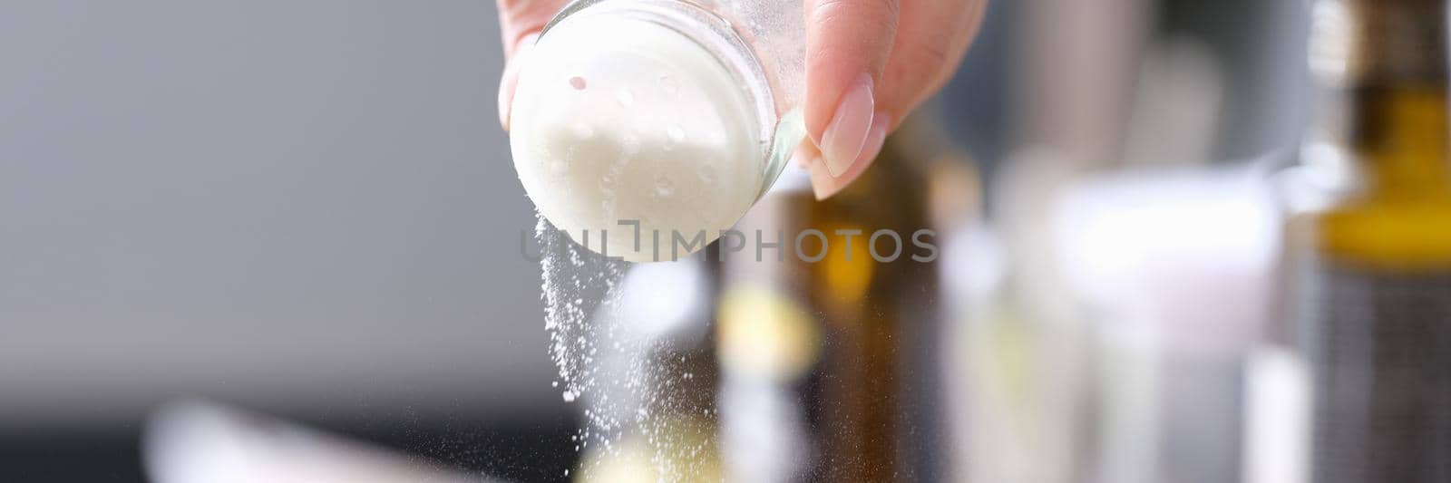 Woman hand pours fine salt into saucepan. Cooking salt control concept